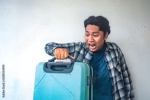 Принти на полотні A man in a plaid shirt holds a blue suitcase with a surprised gesture