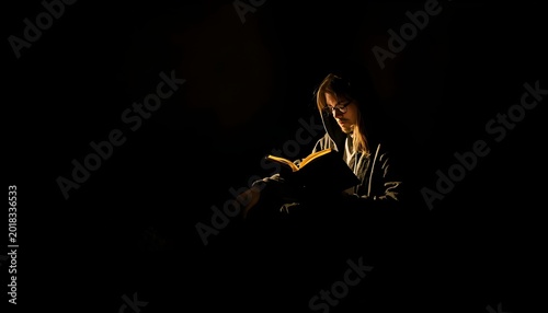 A woman sits in the dark, illuminated only by a small light source