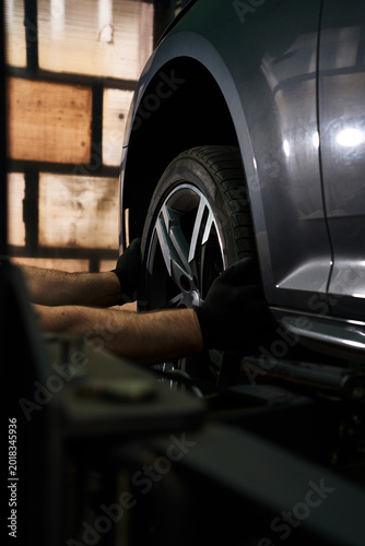 Close-up of a mechanic in black gloves removing a wheel from a modern car at a shop.