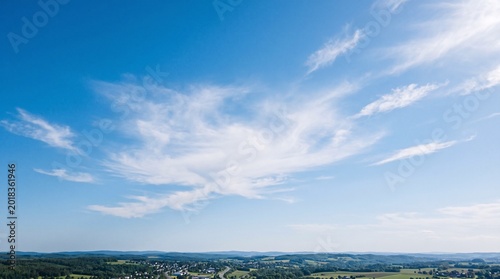 Vast blue sky with delicate wispy white clouds over rural land
