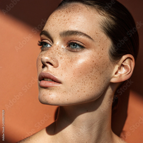 high-quality beauty portrait features a young woman with a striking complexion covered in natural freckles, celebrating authentic skin texture and raw beauty