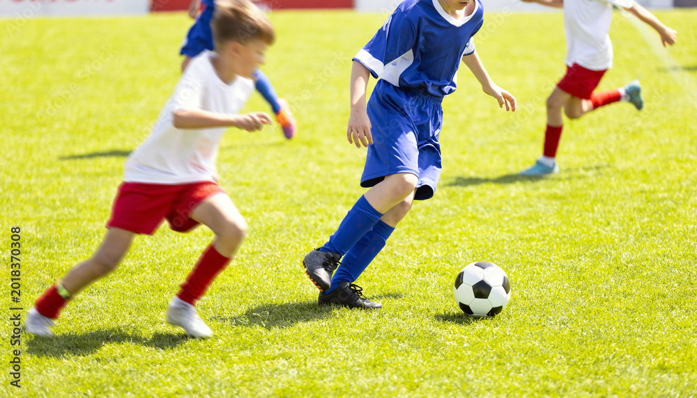 Fototapeta premium Close-Up of Junior Football Players Competing for Ball on Pitch - Youth Soccer Match Action Between Players in Blue and White Uniforms