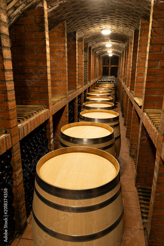 Photography Wine barrels aging in a long arched brick cellar storing bottles