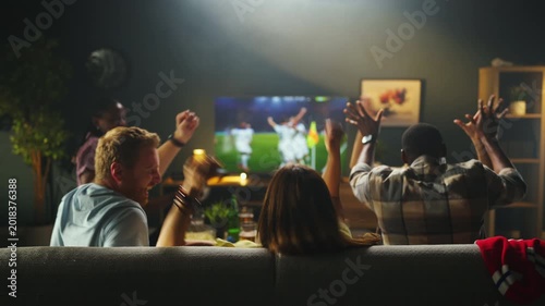 Four friends sit on a couch enjoying a soccer game on TV. They show excitement as they cheer for their teams during the match while eating snacks.