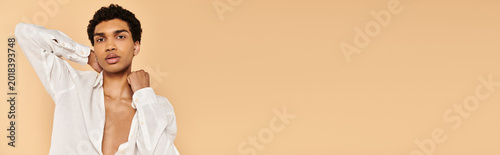 Cuadro en lienzo Vibrant young man poses stylishly against a warm peach background showcasing mod