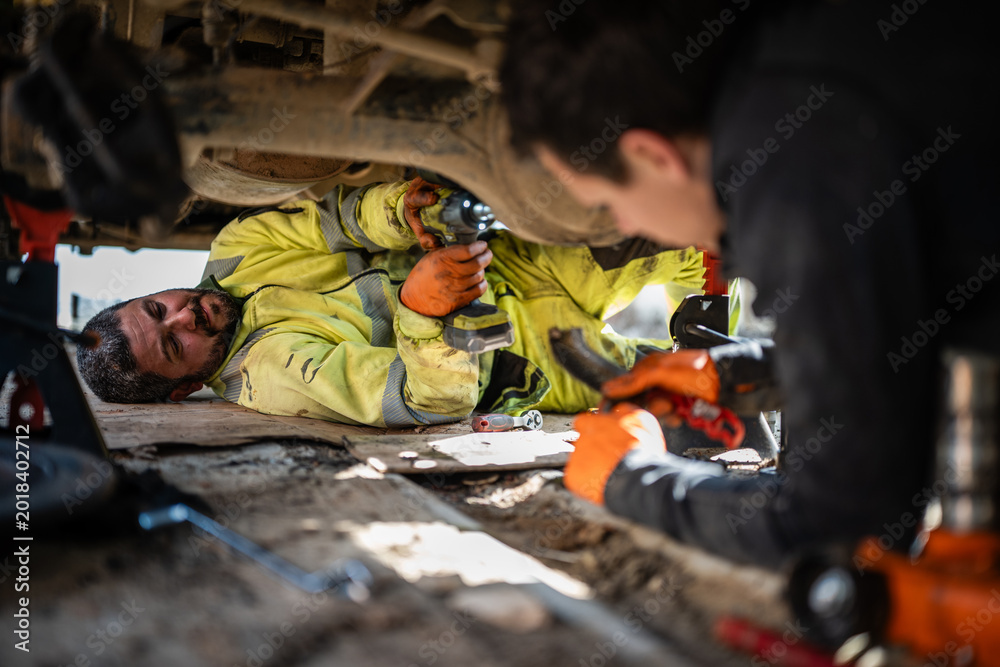 Fototapeta premium Mechanics lying under vehicle performing automotive repair