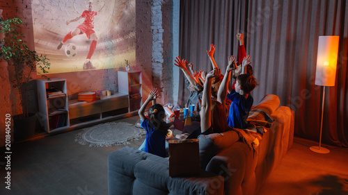 Bilde på lerret Family raising hands while watching soccer projection on brick wall at home