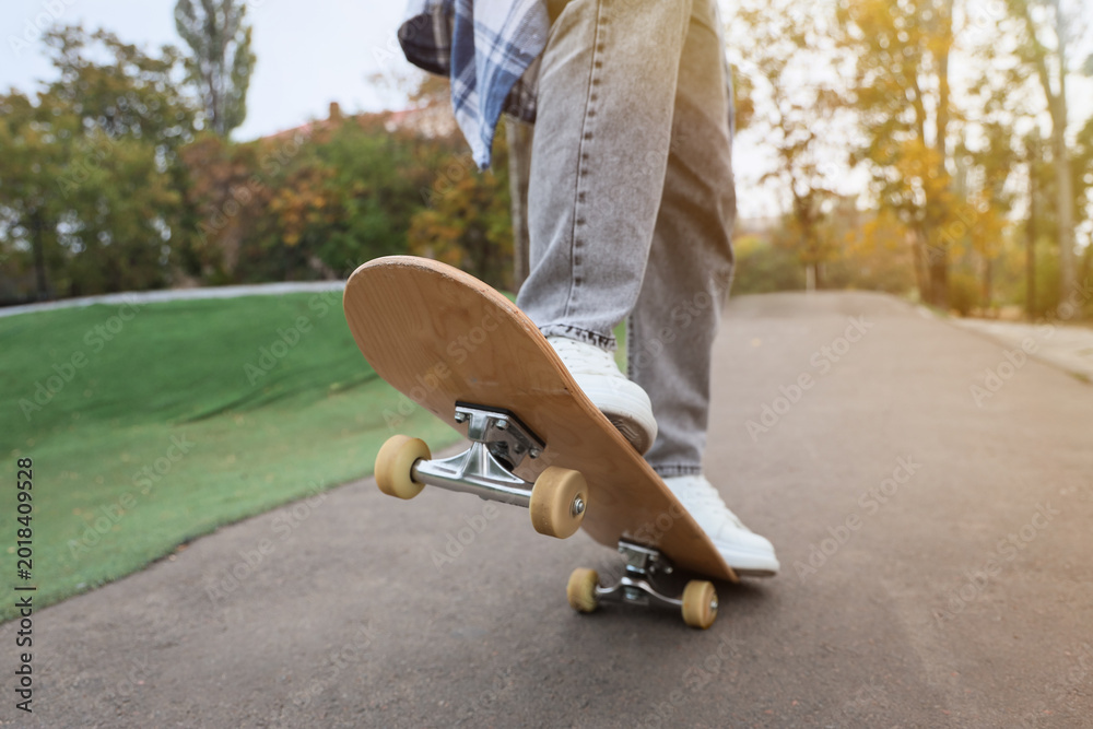 Fototapeta premium Legs of young man with skateboard in park, closeup