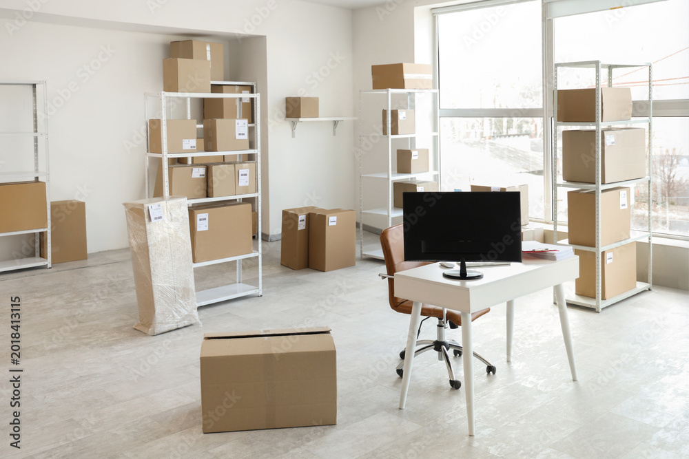 Fototapeta premium Interior of light warehouse with workplace, shelf units and cardboard boxes