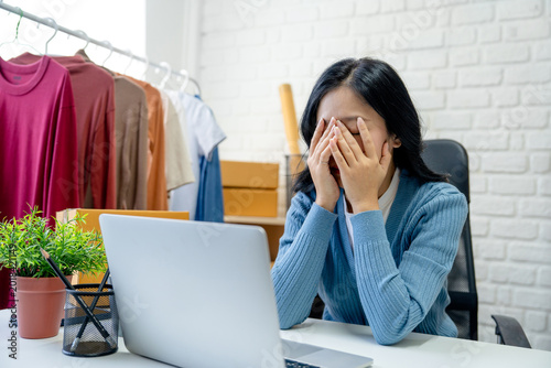 Stressed Asian small business owners working at desks with laptops.