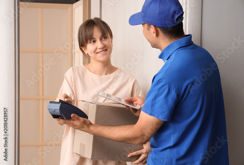 Young woman paying for her parcel via terminal at doorway