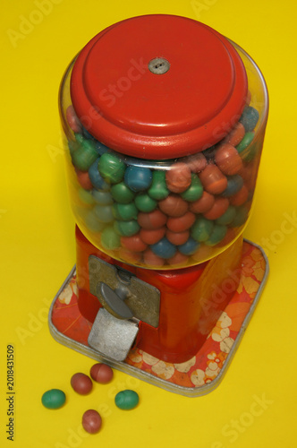 A vintage candy dispenser filled with colorful candies on yellow background