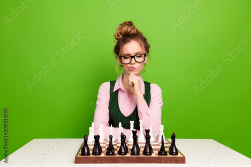 Photography Young student contemplating chess strategy at a table with green background posi