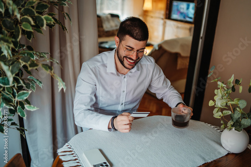 Happy man holding credit card for e-commerce purchase at home