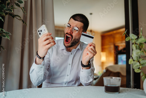 Man yelling holding smartphone and credit card, online payment problem
