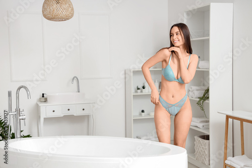 Fotografi Young woman in blue lingerie posing in bright modern bathroom near freestanding