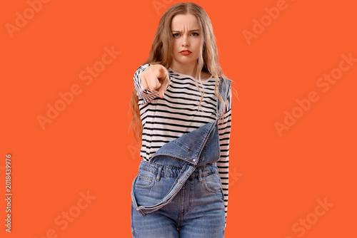 Tableau sur toile Young woman pointing at viewer on orange background