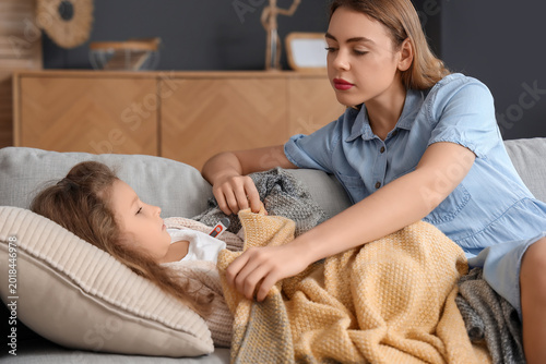 Mother covering her sick little daughter with plaid at home