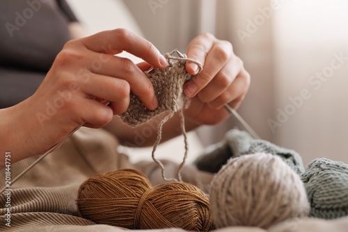 Soft sunlight fills the cozy room as skilled hands work meticulously, knitting threads into a warm fabric. Nearby, colorful yarn balls await their turn in this relaxing craft