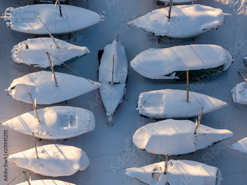 Aerial view of snow-covered sailboats parked on land during winter with golden sunlight and footprints in the snow in Trakai, Vilnius County, Lithuania.