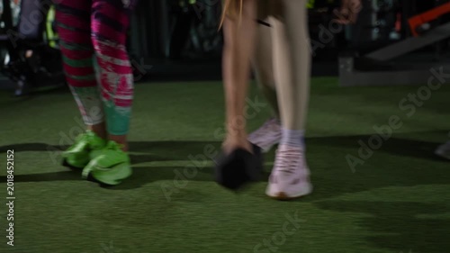 Women's dumbbell fitness workout. Women take turns lifting dumbbells from the green gym floor.