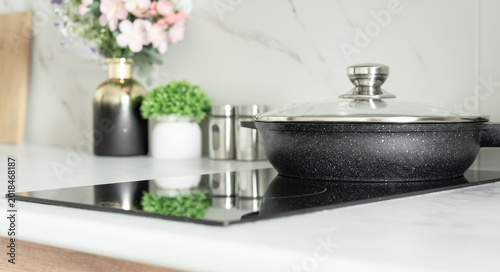 Nonstick frying pan with glass lid on induction cooktop in bright modern kitchen interior.