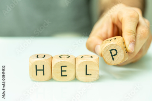 A close-up shot of a hand arranging wooden letter blocks to spell the word help.