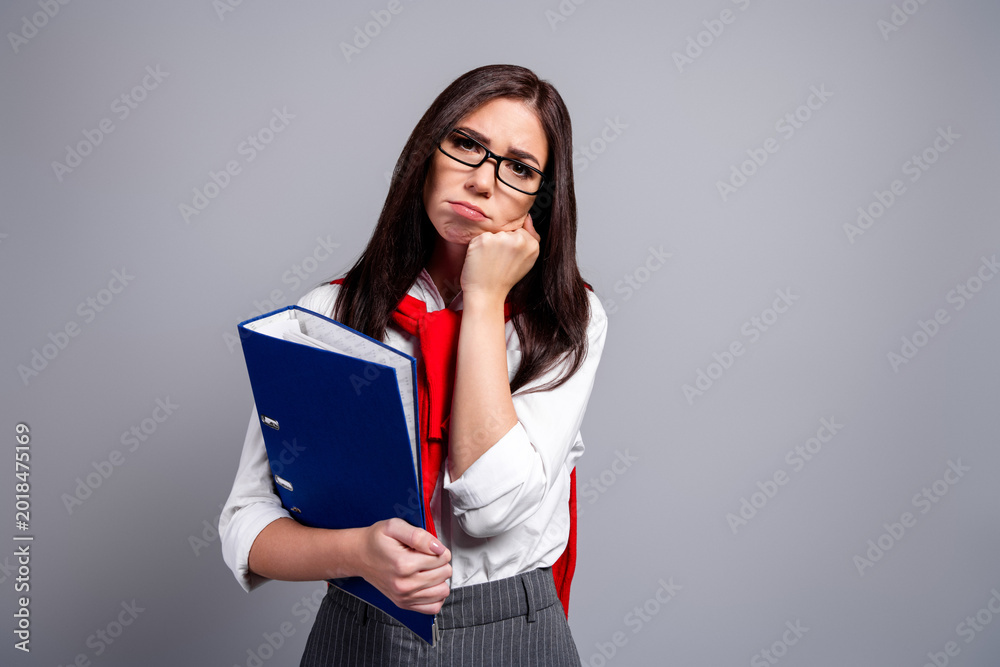 Fototapeta premium Bored student woman with glasses holding blue binder and paperwork, looking tired and frustrated while studying and dealing with documents