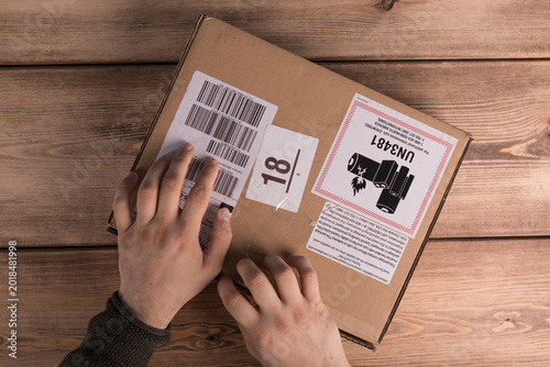 Person's hands carefully holding a cardboard box with shipping labels and UN3481 warning.