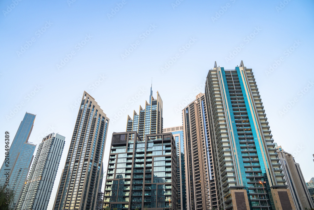 Fototapeta premium Modern skyscrapers rising in dense urban city skyline, tall glass buildings reflecting sunlight, metropolitan architecture, financial district, and contemporary city development concept.