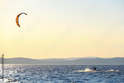 Obraz na plátně kiteboarder on lake balaton with an orange kite above evening water and the tiha