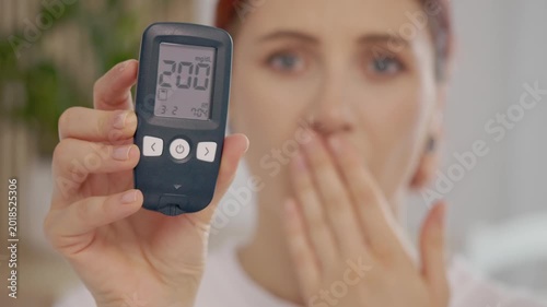 A woman holds a glucometer with a reading of 200 mg dL. This indicates a high blood sugar level that can impact health. Understanding glucose levels is essential.