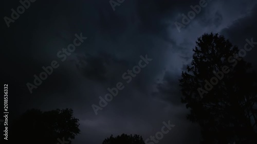 Series of lightning bolts on a dark night sky above the silhouette of trees, captured in slow motion.