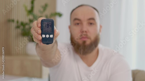 A man holds a glucometer with a reading of 134 mg dL. This reading shows a high blood sugar level. He looks concerned about his health and the implications of diabetes.