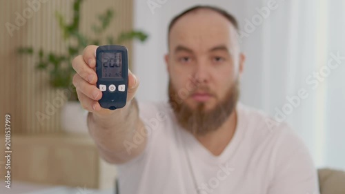 A man holds a glucometer showing a reading of 200 mg dL. He shows concern over the high blood sugar level. This happens in a home environment.