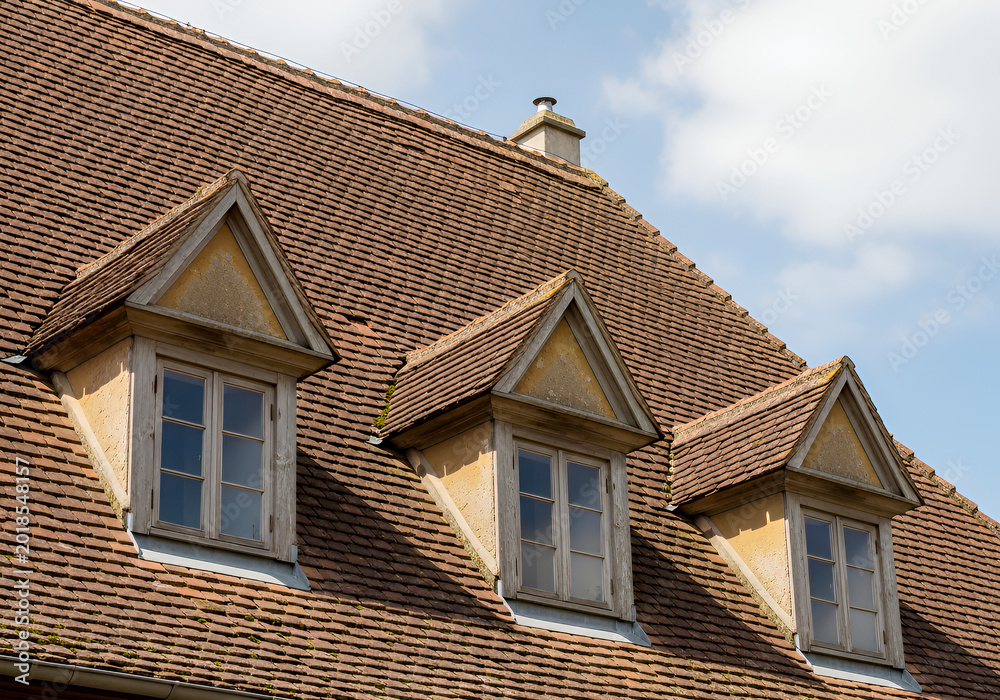 Fototapeta premium Three brown tiled roof dormer windows against a blue sky background brown tiles house