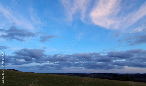A landscape of green earth and trees against a blue summer sky.