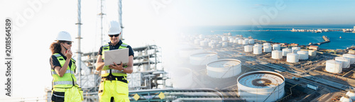 Billede på lærred An engineer reviews data on laptop at sprawling oil refinery, examining large storage tanks and distant harbor while wearing yellow reflective vest and white hard hat on construction platform