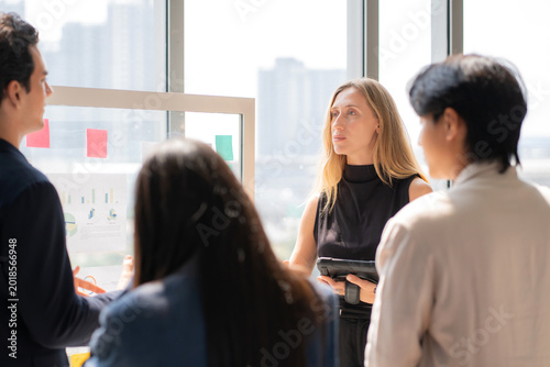 Photos Caucasian businesswoman holding tablet presenting financial report on glass board, colleague team listening during modern office meeting, collaboration and teamwork during project brainstorming