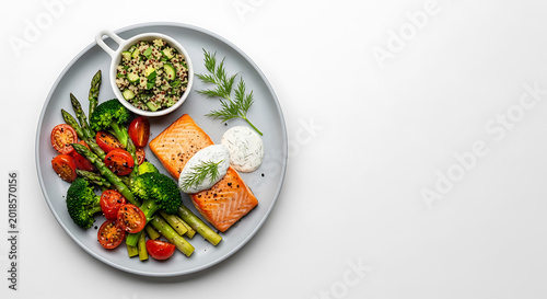 Grilled salmon fillet served with fresh asparagus, cherry tomatoes, broccoli, and a bowl of quinoa salad on a light gray plate, view, white background