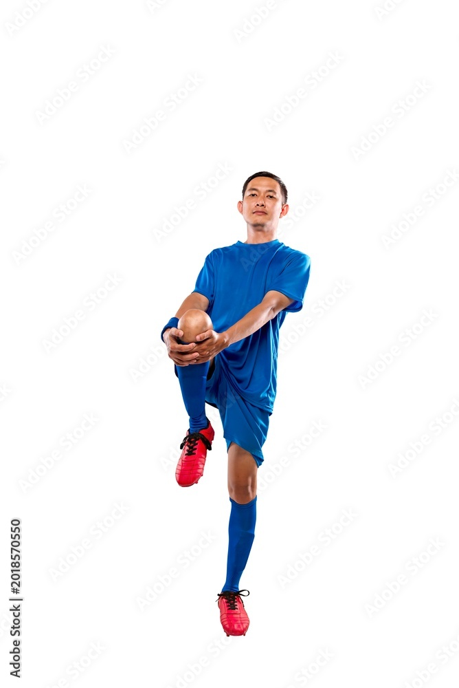 Fototapeta premium Professional Indonesian southeast asian soccer player in blue uniform performing a knee-to-chest leg stretch, isolated on a white background. Ideal for fitness and sports marketing