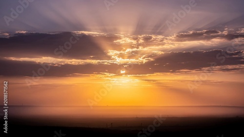 Atmospheric sunset sky with sun rays breaking through layered clouds