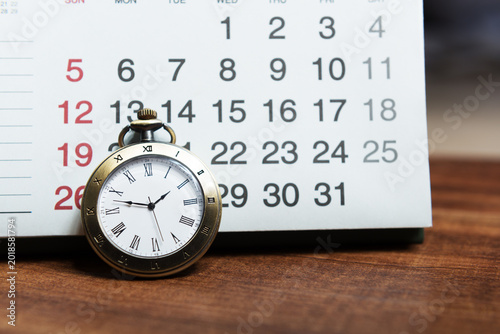 The calendar and pocket watch are on the wooden table.Time is money.