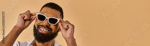 Konstfotografi Vibrant young man showing charm and style while wearing trendy sunglasses indoor