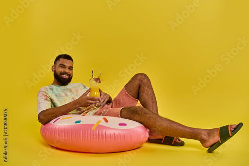 Принти на полотні Vibrant young man enjoys a refreshing drink while relaxing on a colorful float