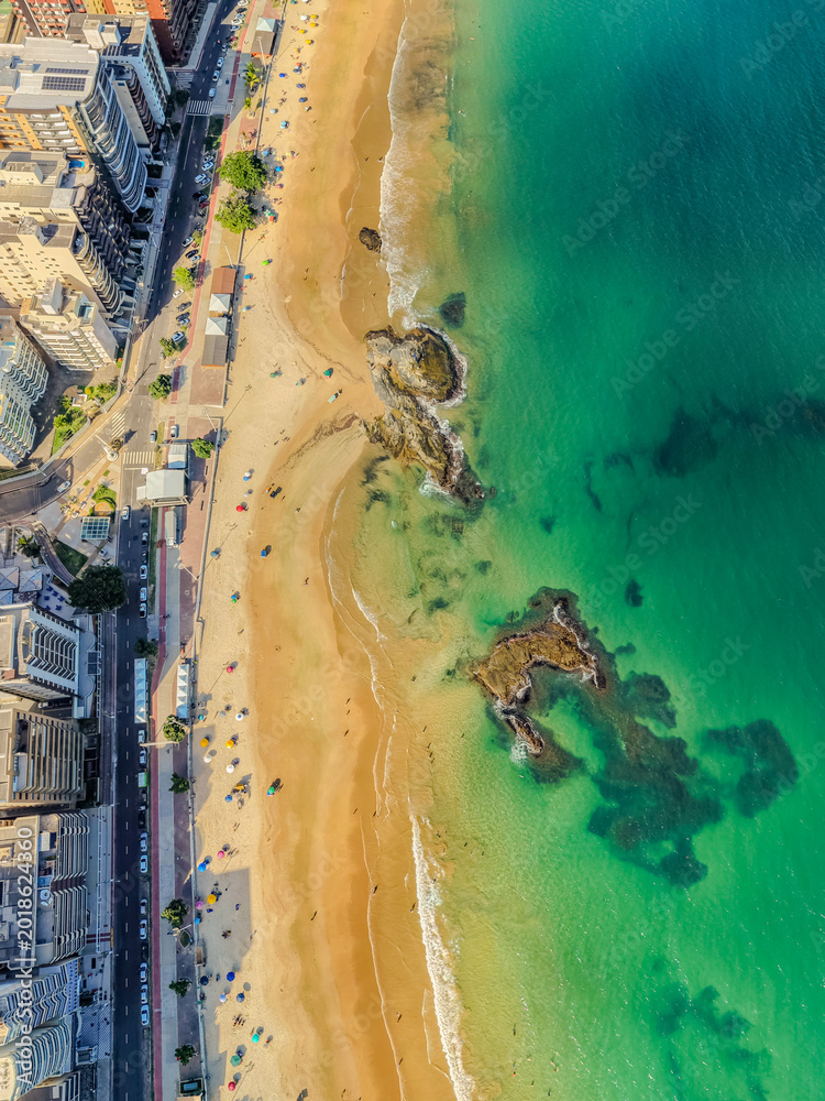 Naklejka premium Aerial drone view of Praia do Morro beach crowded with tourists during the summer high season in Guarapari, Espírito Santo, Brazil. Urban coastline with colorful umbrellas, Atlantic Ocean and city sky