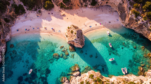 Stunning aerial view of a secluded cove with crystal clear turquoise water and boats anchored offshore.