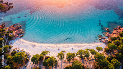 Aerial view of a stunning tropical beach with turquoise water and lush green trees during sunset.