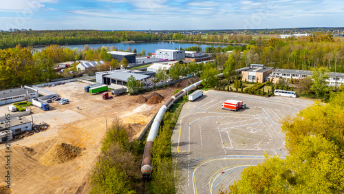 Foto Aerial photograph showing an industrial zone with a driving school maneuver yard, a railway siding with a long train of tank wagons, warehouse buildings, a lake, and forest