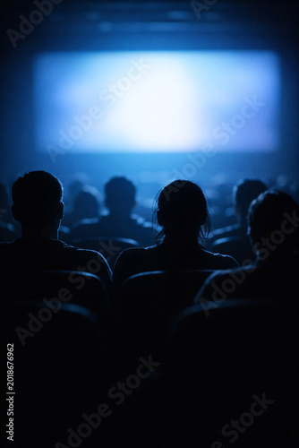 Silhouette of people sitting in a darkened movie theater watching a film